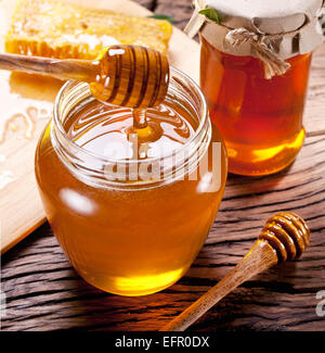 Honey dripping from wooden spoon into glass can. Stock Photo