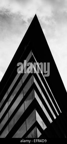 Black and white photo looking up at pointed glass facade with roof overhang and clouds beyone Stock Photo