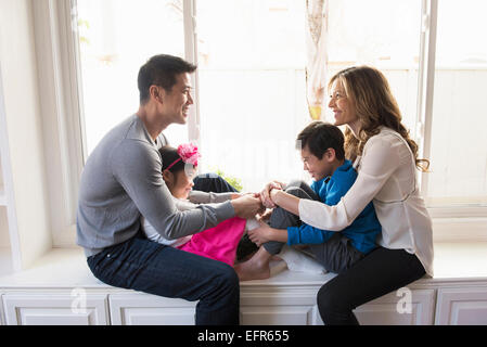 Mature couple and two children sitting on living room window seat Stock Photo