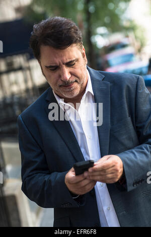 Mature businessman walking on street texting on smartphone Stock Photo