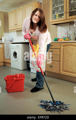 Young woman, house wife cleaning her kitchen. Mopping the floor, polishing the table and general housekeeping and dusting. Stock Photo