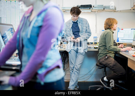 Three people at a computer repair shop, one checking his smart phone. Stock Photo