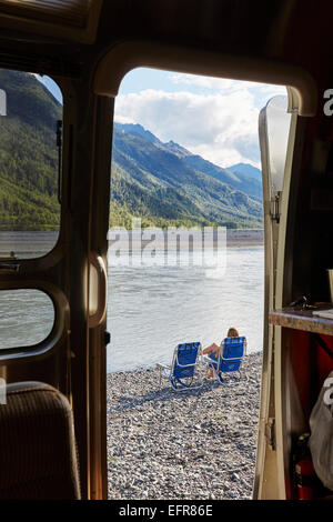 View from camper van doorway of mid adult woman sitting by lake, Palmer, Alaska, USA Stock Photo