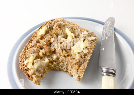 Slice of Freshly Baked Warm Wholemeal Bread with Butter with Bite Taken on a Plate with a Knife Stock Photo