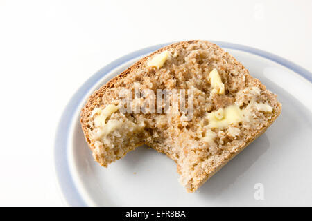Slice of Buttered Freshly Baked Warm Wholemeal Bread with One Bite Taken on a Plate Stock Photo