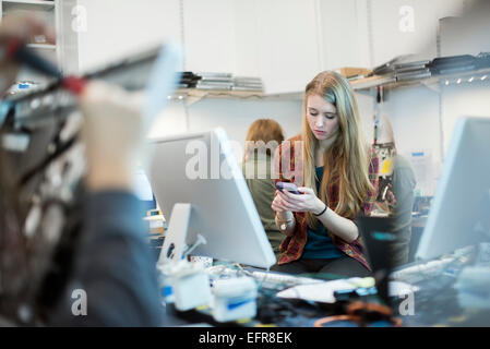 Computer Repair Shop. A woman using a smart phone.  People working on computer repairs. Stock Photo