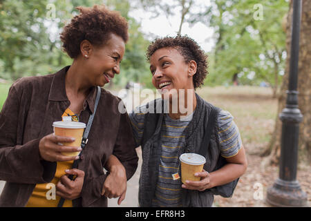 Two mature female friends drinking takeaway coffee whilst strolling  in park Stock Photo