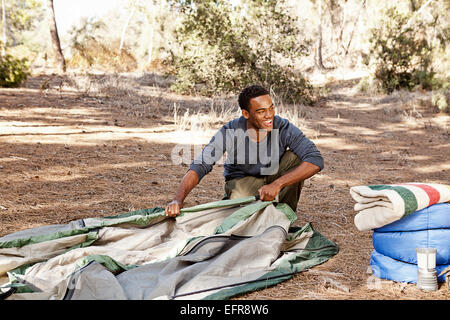 Young man kneeling in forest putting up tent Stock Photo