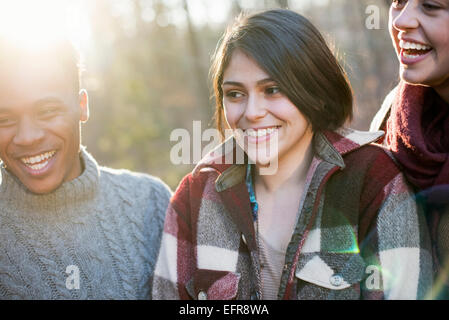 A woman and two men smiling, standing in a sunlit forest in autumn. Stock Photo