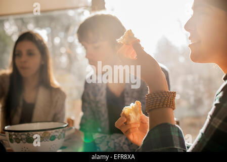 Three people sitting at a table, smiling, eating and chatting. Stock Photo