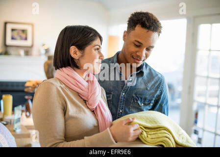 Smiling couple standing in a living room, woman holding a yellow blanket. Stock Photo