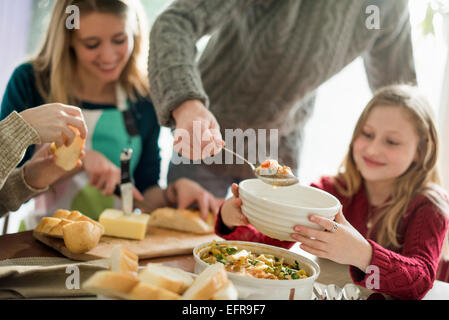 Four people sitting and standing at a table, a man serving food into a bowl. Stock Photo