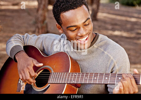 Young man sitting in forest playing acoustic guitar Stock Photo