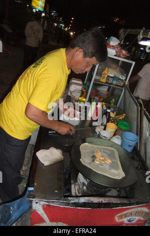 Vertical portrait of a street vendor busy making fresh pancakes on the roadside at night Stock Photo