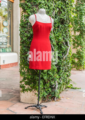 A red dress displayed on a manikin outside a store against a green ivy covered wall in Santa Barbara, California. Stock Photo
