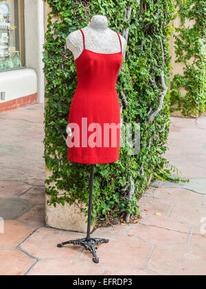 A red dress displayed on a manikin outside a store against a green ivy covered wall in Santa Barbara, California. Stock Photo