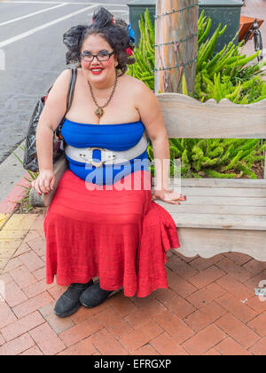 An obese twenty something woman dressed in bizarre red, white and blue outfit sitting on a bench in Santa Barbara, California. Stock Photo