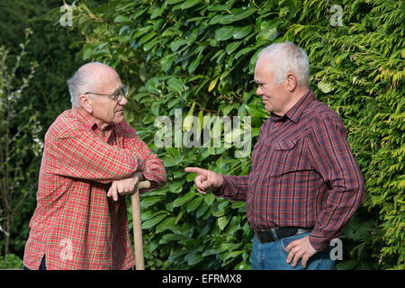 two senior men standing in garden and descussing, one is holding spade Stock Photo