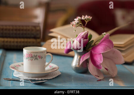 A pretty coffee cup and a opened book on a wooden table Stock Photo