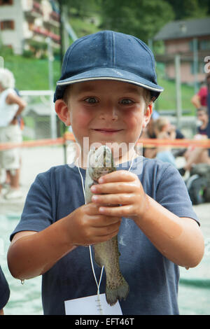 A young boy fisherman proudly examines the rainbow trout he caught