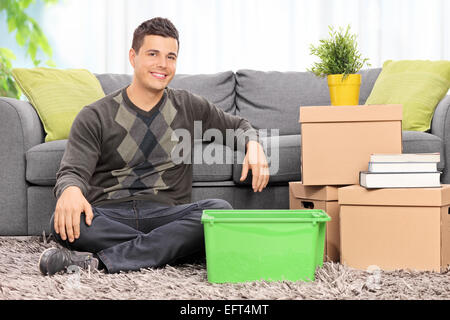 Man seated on the floor by a bunch of boxes at home Stock Photo