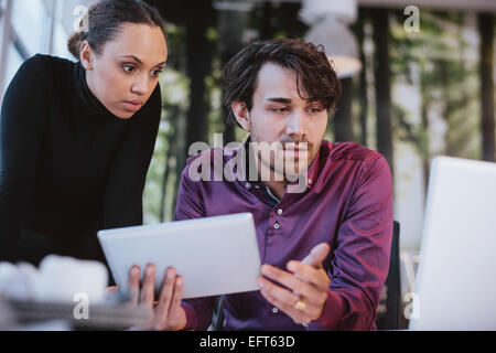 Two young business professionals working together on a project. Creative executives using digital tablet and laptop for research Stock Photo