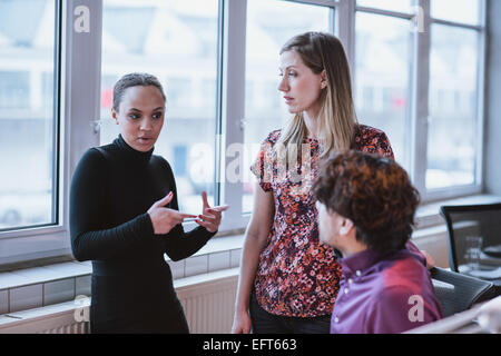 Young woman explaining business strategy to colleagues. Multiracial businesspeople discussing work in office. Stock Photo
