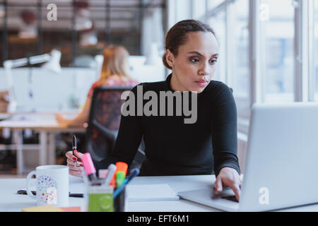 Image of young woman working on laptop while sitting at her desk in modern office. African female executive at work. Stock Photo