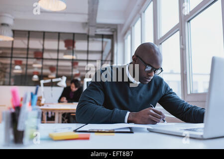 African male executive taking notes. Young businessman working at his desk. Stock Photo