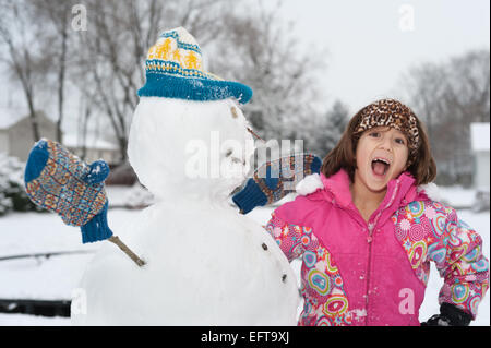 young girl with a snowman who is wearing a knit hat and gloves Stock Photo