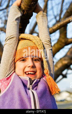 Young girl swinging on a tree branch in the autumn wearing knitted stocking cap. Stock Photo