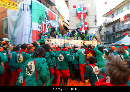 A cart passes through the narrow streets of the ancient city as other teams surround it throwing oranges during Ivrea Carnival Stock Photo