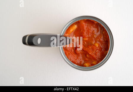 An opened can of inexpensive pasta in tomato sauce with a black handle spoon atop a white table top with natural window light. Stock Photo