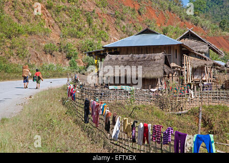 Burmese man carrying firewood on his back and laundry drying on fence in rural village, Tachileik District, Shan State, Myanmar Stock Photo