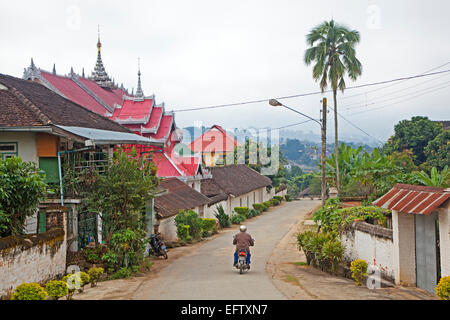 Motorcyclist riding past Buddhist temple in the town Keng Tung / Kengtung, Shan State, Myanmar / Burma Stock Photo