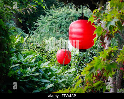 Red and white paper lanterns hung in a beautiful, peaceful leafy garden.  Celebrations, new year, party decorations. Stock Photo