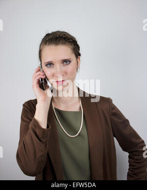 Beautiful young business woman wearing brown jacket uses cell phone Stock Photo