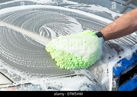 A man uses a soft, green micro fiber mitt with soapy water to wash his car. Stock Photo