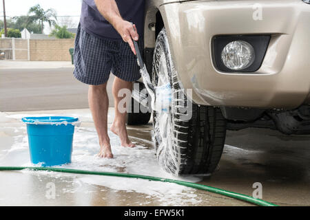 A man washing his car uses a soapy brush to clean the tires and wheels of his vehicle. Stock Photo