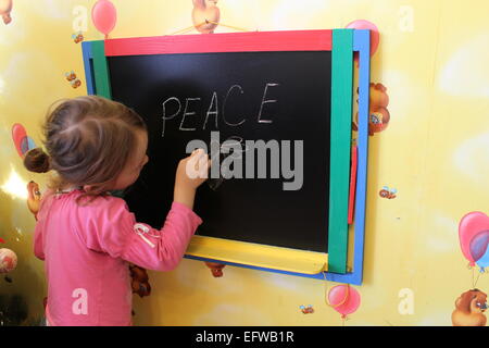 little girl writes on blackboard word Peace Stock Photo