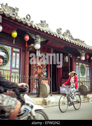 Woman riding bicycle by the Quan Cong temple (Chua Ong), Hoi An, Vietnam. Stock Photo
