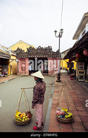 Woman carrying baskets by the Japanese bridge, Hoi An, Vietnam. Stock Photo