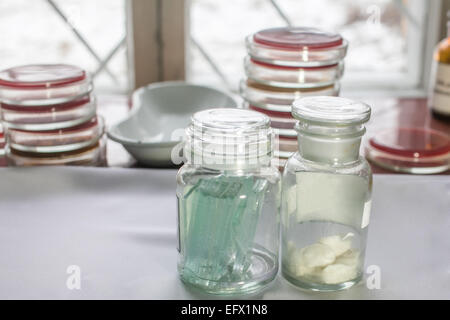 Bottles with glass pieces and swabs in a lab; Petri dishes stacked on the background Stock Photo