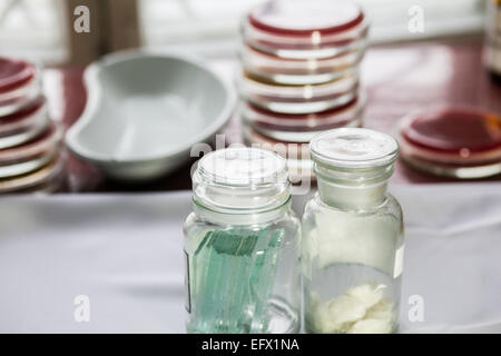 Bottles with glass pieces and swabs in a lab; Petri dishes stacked on the background Stock Photo
