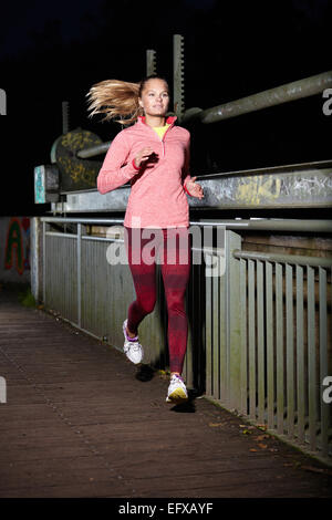 Young woman running on footbridge at night Stock Photo