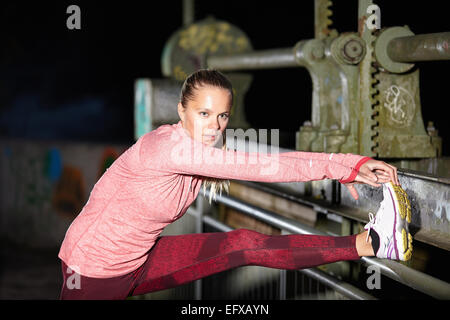 Young woman touching toes on footbridge at night Stock Photo