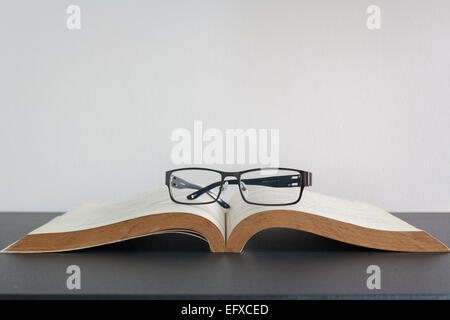 Open book and eyeglasses on desk Stock Photo