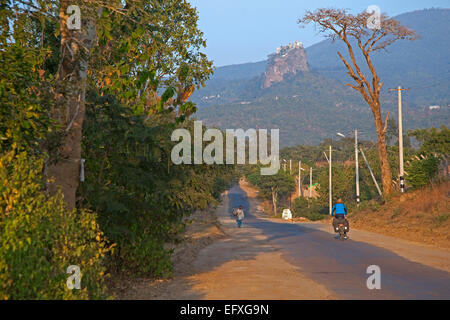 Tourist cycling towards Buddhist monastery on summit of Taung Kalat near  volcano Mount Popa, Mandalay state, Myanmar / Burma Stock Photo