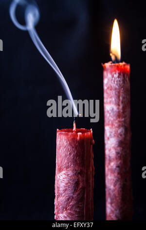 blown out candle flame showing nice smoke in a dark background, other candle remains lit with flame Stock Photo