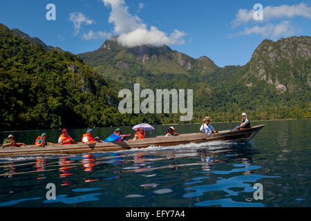 A boat carrying tourists is sailing on sea water in a background of the landscape of Seram Island near Saleman village in North Seram, Central Maluku, Stock Photo